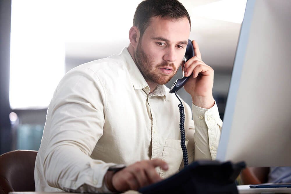 Business professional dialing an office phone using business phone services