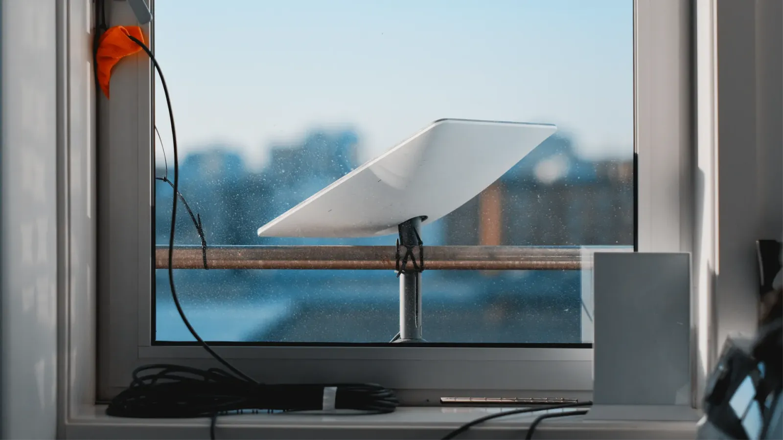 Satellite internet dish mounted outside an apartment window, with its cable and router on the windowsill